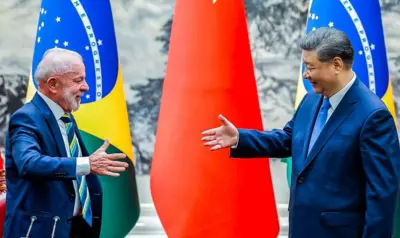 Foto mostra Lula, à esquerda, e Xi Jinping, à direita, com as mãos levantadas segundos antes de apertarem as mãos