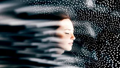 На изображении крупный план лица женщины с закрытыми глазами. Вокруг — художественный эффект, создающий иллюзию движения и света. Фон тёмный, усеян множеством мелких белых точек.