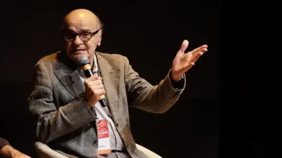 Drauzio Varella sentado e gesticulando enquanto fala ao microfone
