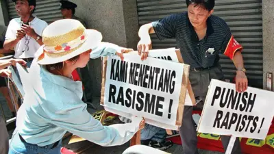 Plakat dengan tulisan "Kami menentang rasisme!" dan "Menghukum para pemerkosa!", di depan Konsulat Indonesia di Hong Kong, 26 Juli 1998.
