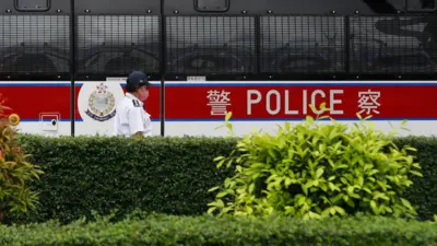 2023年6月24日,一輛警車在香港維多利亞港執勤,一名警員在警車前走過。