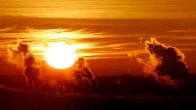 A bright sun creates a red sky over the industrial chimney stacks of Grangemouth