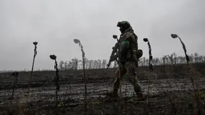 Украинский военный в форме и с автоматом идет по полю.