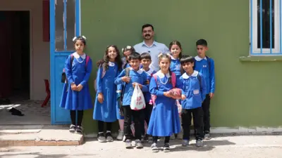 Manap ve öğrencileri okulun önünde poz veriyor. Öğrencilerin üzerinde beyaz önlüklü mavi üniformalar var.