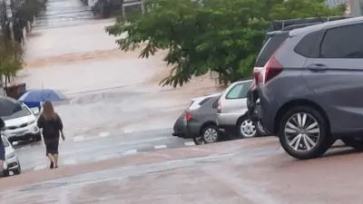 Mulher caminhando na rua com guarda-chuva; na frente dela, está grande volume de água