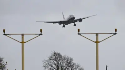 A British Airways plane coming in to land with two electrical cable structures in front of it