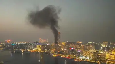 Escena nocturna de la costa de Dubái que muestra una columna de humo negro espeso que se eleva desde un grupo de edificios.