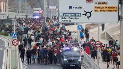 Spanyol rendőrök és katonák egy nagy csoport bevándorlót kísérnek Ceutában a határhoz, hogy kivezessék őket Spanyolországból.