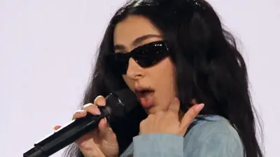 Charli XCX in dark glasses singing into a microphone