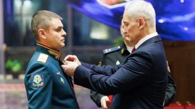 Седой мужчина в костюме прикалывает награду к груди мужчины в парадной военной форме
