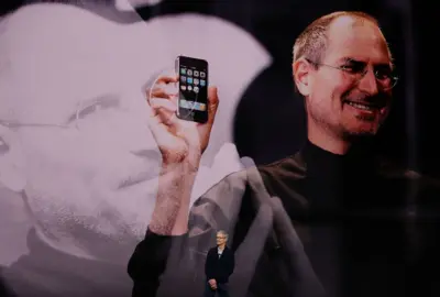 12 Eylül 2017'de Kaliforniya, Cupertino'daki Apple Park kampüsünde bulunan Steve Jobs Tiyatrosu'nda düzenlenen Apple özel etkinliğinde konuşma yapan Apple CEO'su Tim Cook, siyah ceket ve beyaz gömlek giymiş halde, Apple logosu ve gözlüklü, elinde bir iPhone tutan Apple'ın kurucu ortağı Steve Jobs'un yer aldığı bir arka plan görüntüsünün önünde, ellerini kavuşturmuş bir şekilde sahnede duruyor.