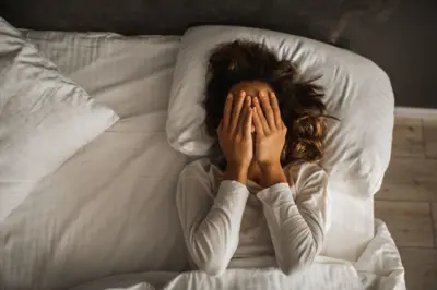 Mulher deitada na cama cobrindo o rosto com as mãos