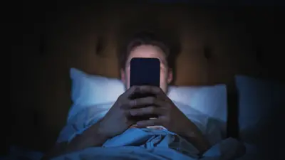 男性がベッドに横になり、枕に頭を乗せて、スマートフォンを操作している