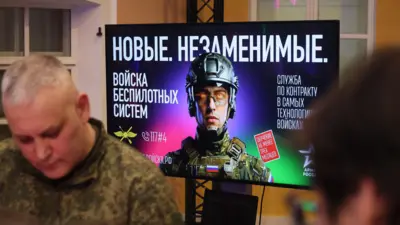 На переднем плане мужчина в камуфляже, на заднем, на большом экране, - реклама службы в беспилотных войсках