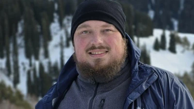 Иаков Воронцов позирует на фоне гор, на нем черная шапка и синяя ветровка