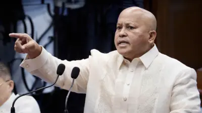 Ronald Dela Rosa, seorang pria berkepala botak mengenakan kemeja berkancing berwarna krem, duduk dan menatap ke kejauhan.