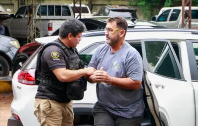 Homem com algemas na mão sendo retirado de carro por policial