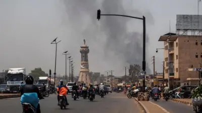 A column of black smoke rises above buildings as traffic passes the Africa Tower monument in Bamako on April 26, 2026