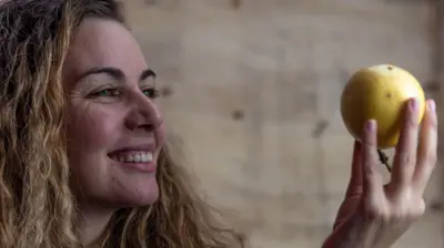 Una mujer sonriente mira un maracuyá que sostiene en la mano