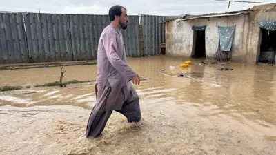حویلی قدیمی که پر از آب سیلاب است و یک مرد که تا زانویش در آب است در حال قدم زدن است.