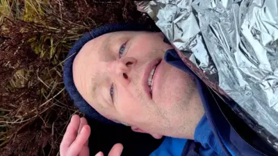 Glenn Campbell lying on the ground looking up at the camera, with a foil blanket over him.