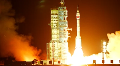 A Long March-2F rocket carrying the Shenzhou-19 spacecraft takes off.  Orange flames shoot out of the rocket launcher.