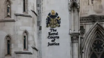白いゴシック様式の建物にイギリスの国章が掲示され、その下に「The Royal Courts of Justice」と書かれている