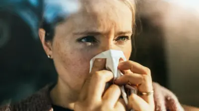 Bir kadın burnunu kağıt mendille siliyor.