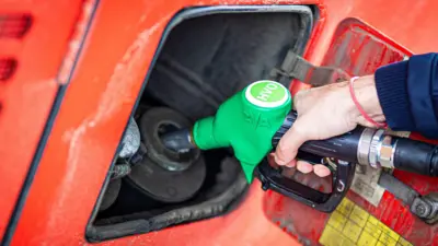 Close-up shot of a red bus being refuelled via a green pump, labelled HVO. A person's hand and blue sleeve is visible holding the pump.