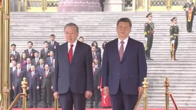 蘇林（左）與習近平（右）在北京人民大會堂前檢閱台站立，參加中國官方歡迎蘇林儀式（中國中央電視台片段截屏 15/4/2026）