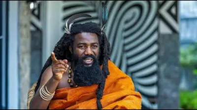 Umugabo wambaye umwitero ukoze mu ruhu rwa orange, afite imisatsi miremire ikaraze n'amababa mu mutwe