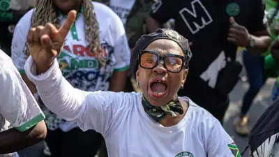 A woman in a black beret and sunglasses shouts and waves her finger in the air.