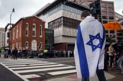 Um homem, com uma bandeira israelense em frente ao local onde dois funcionários da embaixada israelense foram mortos em Washington DC, no dia 22 de maio de 2025
