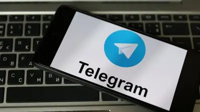 Колаж, на якому смартфон із заставкою телеграма лежить на темній клавіатурі ноутбука.