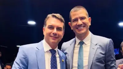 Flávio Bolsonaro e Douglas Ruas posam para foto sorridentes, ambos de terno e gravata azuis