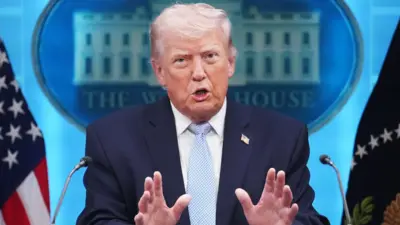 ダークスーツ姿のトランプ氏がホワイトハウスの記者会見場でマイクを前に立ち、両手を前に突き出して口を開いている