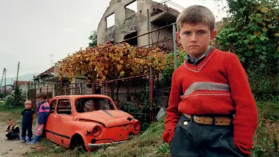 Мальчик стоит рядом с разрушенным домом на востоке Боснии в 1995 году.
