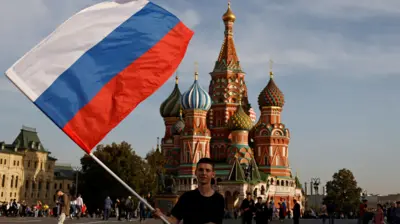 Jovem agita bandeira russa na frente da praça Vermelha,vaidebet suporteMoscou