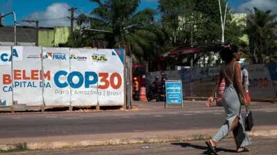 Ayol iqlim bo'yicha konferentsiyani e'lon qiluvchi plakat yonidan o'tmoqda.