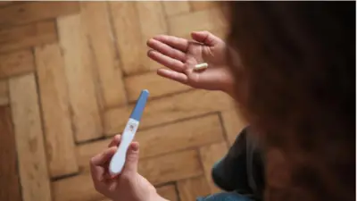 妊娠検査薬と薬のカプセルを眺める長髪の女性を、上から写しているイメージ写真