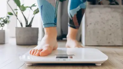 A woman in gym clothing steps on to electronic weighing scales at home