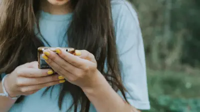 A teenage girl with yellow nail polish on a smartphone