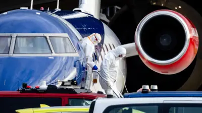 Pessoas usando roupas protetoras durante o desembarque de um avião