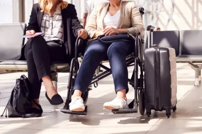 Businesswoman Sitting In Airport Departure With Female Colleague In Wheelchair (stock image)