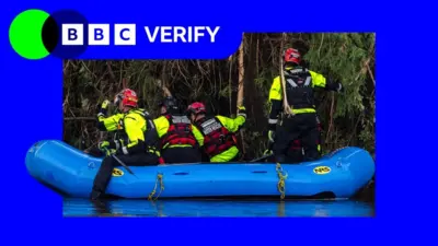 テキサス州の川に青色のボートが浮かび、その上に救助隊員4人が乗っている。全員がヘルメットをかぶり、黄色の上着と赤い救命胴衣を着けている