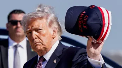 屋外に立つトランプ氏。手に、「アメリカ湾」と書かれたキャップを持っている