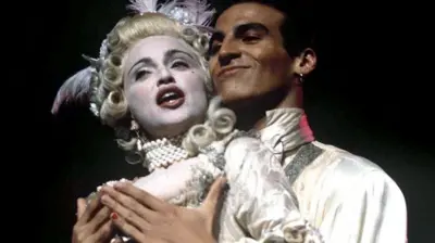 Salim sorrindo atrás de Madonna, que canta com figurino de Marie Antoinette; eles estão com os corpos próximos