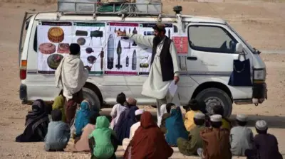 تصویر یک تیم آگهی دهی از خطرات ماین که در یک روستا به کودکان آگهی دهی میکنند. آن ها تصاویر مهمات منفجر ناشده را به کودکان نشان میدهند. کودکان نیز در روی زمین نشسته و به آنها گوش میدهند.