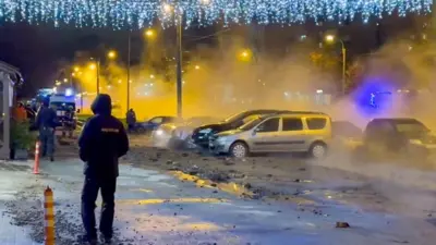 Прорыв трубы в Санкт-Петербурге в декабре 2025 года: ночная улица с новогодними украшениями на столбах и горящими фонарями, спецтехника на заднем плане. В воздухе пар