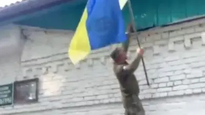 A still from footage shared on social media appears to show Ukrainian soldiers lifting their national flag while climbing a wall up to a tin roof of a building in Guevo, Kursk oblast on 11 August